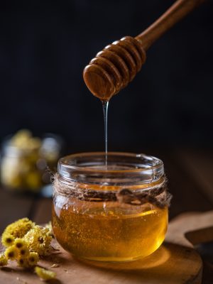 Natural floral honey drains to jar on wood background. Front view Mad Rock Honey-1kg